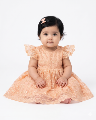 baby sitting wearing peach lace dress with cap sleeves
