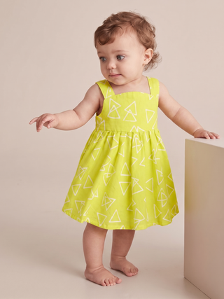 Baby wearing a yellow dress with white triangle patterns on a beige background