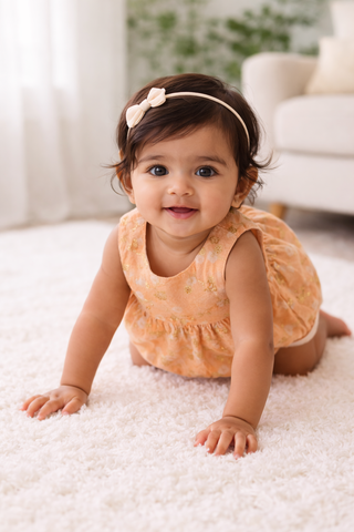Baby in an orange dress crawling on a white carpet